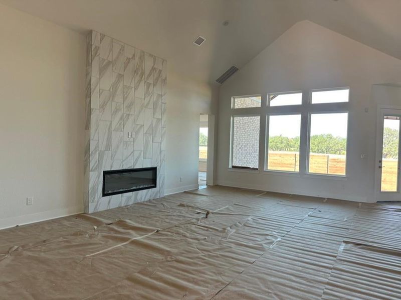Unfurnished living room featuring high vaulted ceiling and a tiled fireplace