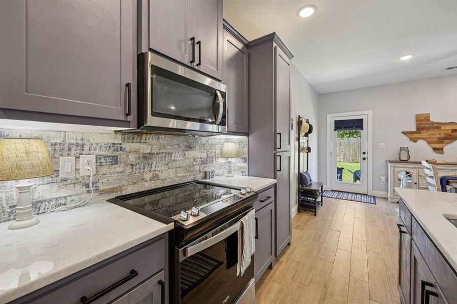 Kitchen with appliances with stainless steel finishes, backsplash, light stone countertops, light wood-type flooring, and recessed lighting Kitchen with appliances with stainless steel finishes, backsplash, light stone countertops, light wood-type flooring, and recessed lighting
