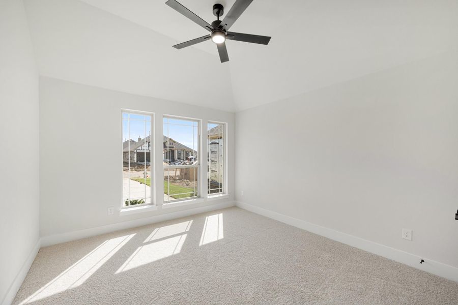 Empty bedroom with carpet flooring, ceiling fan, vaulted ceiling, and three windows with neighborhood view