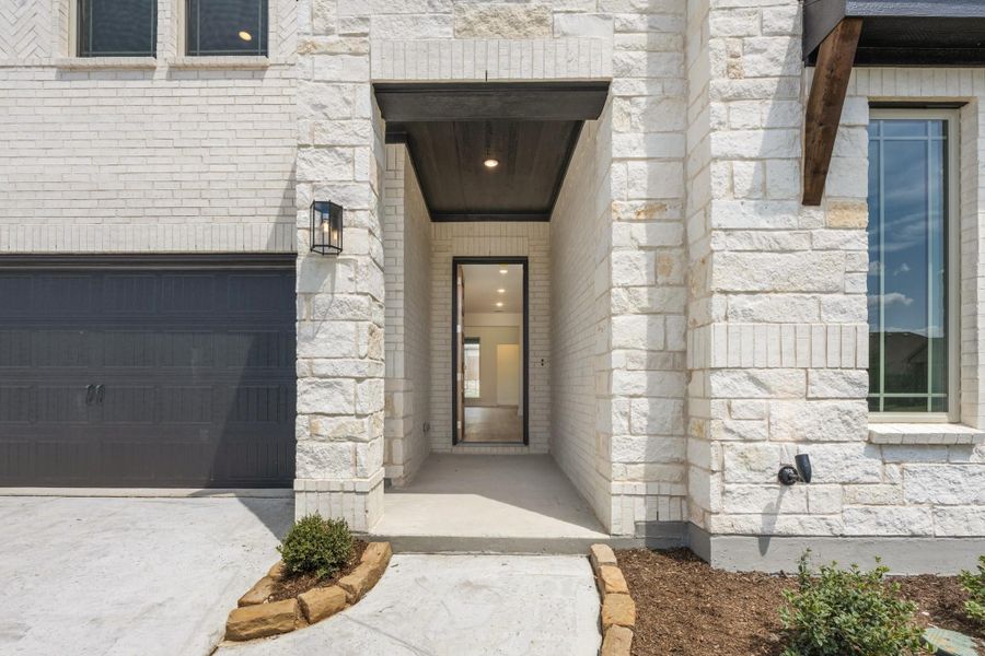 Home entrance with white brick and stone exterior, covered entryway, dark front door, and attached garage