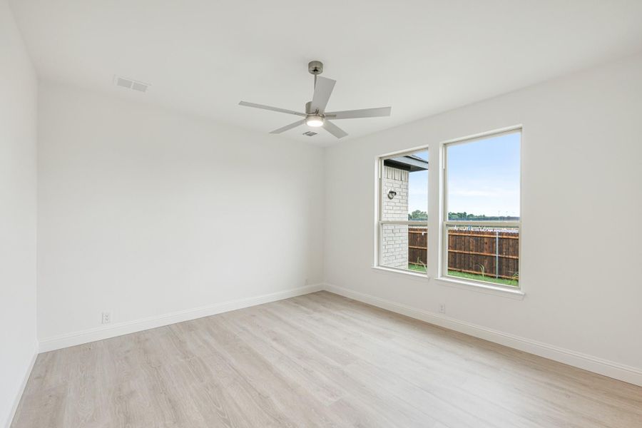 Empty bedroom with light wood floors, ceiling fan, and two windows overlooking backyard fence Empty bedroom with light wood floors, ceiling fan, and two windows overlooking backyard fence