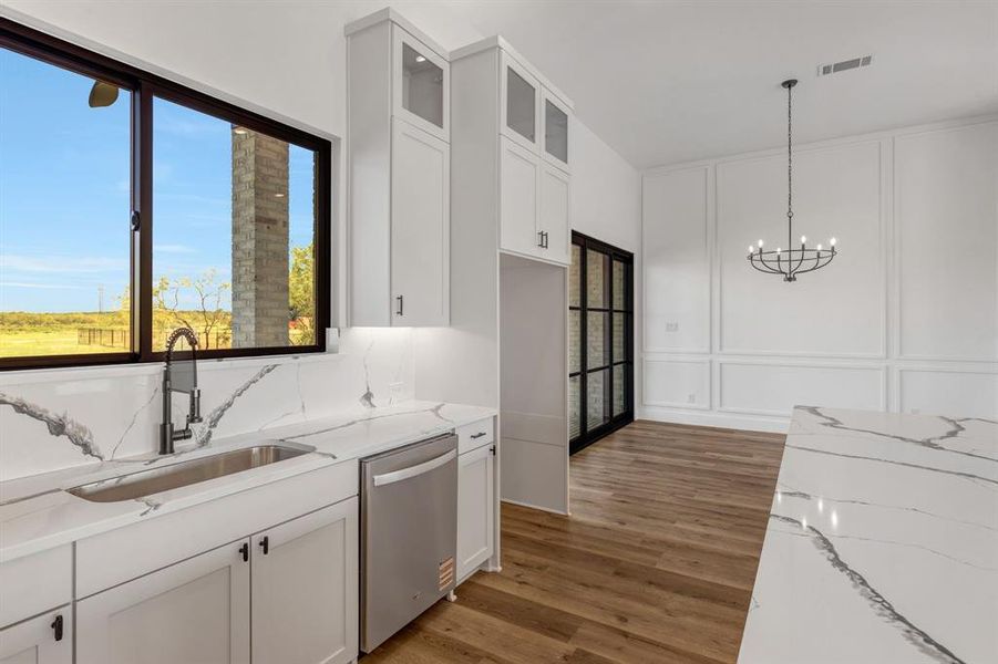 Kitchen featuring a decorative wall, white cabinetry, glass insert cabinets, light stone counters, and dishwasher