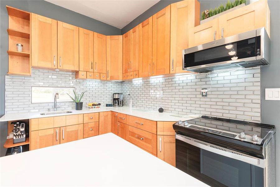 Kitchen with open shelves, stainless steel appliances, tasteful backsplash, and light brown cabinetry Kitchen with open shelves, stainless steel appliances, tasteful backsplash, and light brown cabinetry