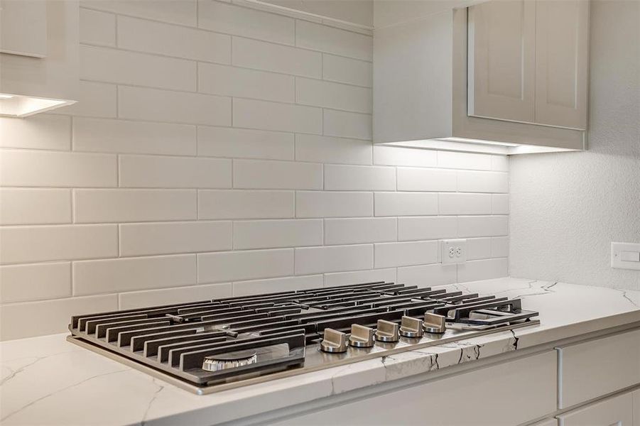 Interior details featuring stainless steel gas stovetop, decorative backsplash, and light stone countertops