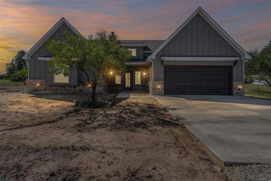 View of front facade with board and batten siding, stone siding, concrete driveway, a garage, and roof with shingles