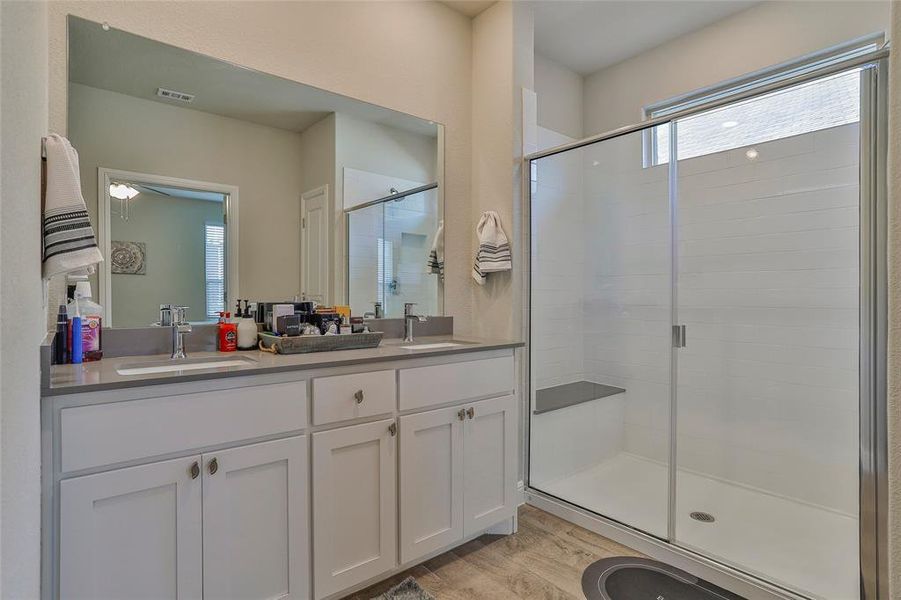 Full bath featuring a stall shower, double vanity, and light wood-style flooring Full bath featuring a stall shower, double vanity, and light wood-style flooring