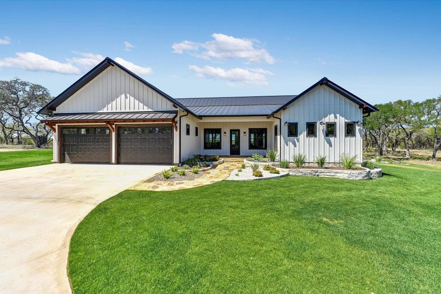 Custom built home featuring a standing seam roof, board and batten siding, a garage, concrete driveway, and a porch