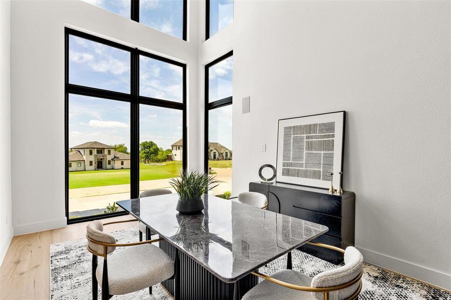 Two-story window wall with black trim, light wood-finish flooring, white walls, and a built-in wall speaker