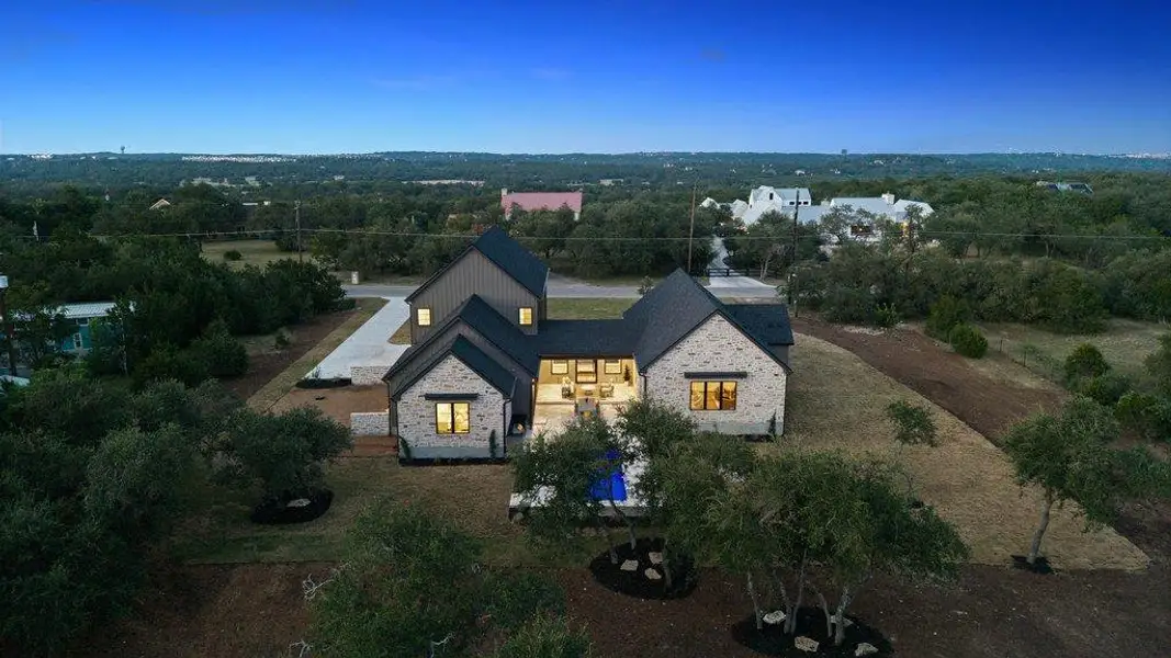An aerial view showcases this modern home's striking blend of stone and dark siding, nestled within a verdant, expansive landscape.