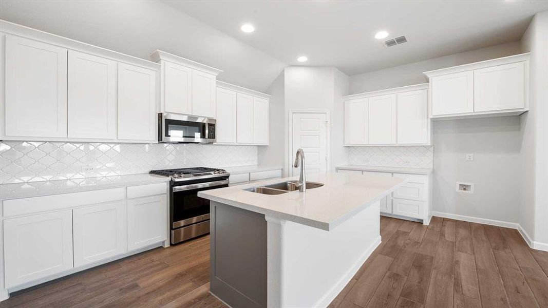 Kitchen featuring stainless steel appliances, sink, backsplash, light wood-type flooring, and white cabinetry