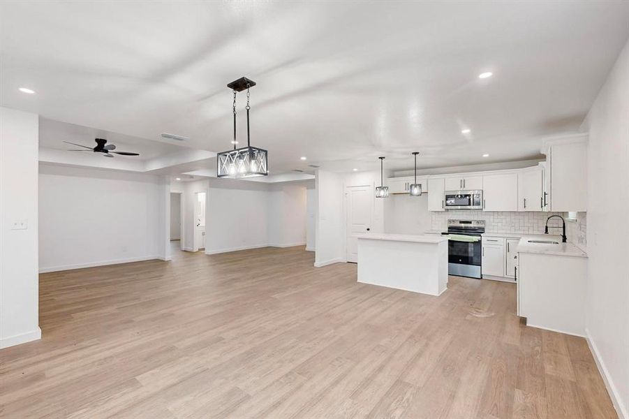 Kitchen featuring appliances with stainless steel finishes, light wood-type flooring, decorative light fixtures, white cabinets, and a kitchen island