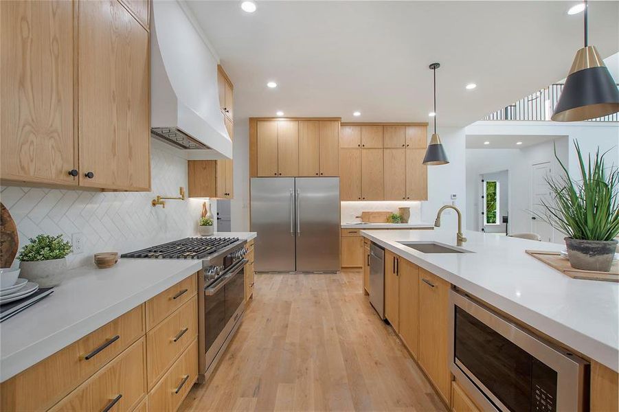 Kitchen featuring built in appliances, a sink, premium range hood, light brown cabinets, and light countertops Kitchen featuring built in appliances, a sink, premium range hood, light brown cabinets, and light countertops