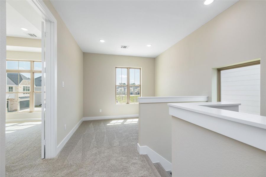 Step into the bright and inviting flex space at the top of the stairs, where soft carpeting and neutral walls create a warm atmosphere. Natural light pours in through multiple windows, and a view into an adjacent room with large windows enhances the open feel. This versatile area offers endless possibilities — whether used as a study nook, play zone, or flexible living space.