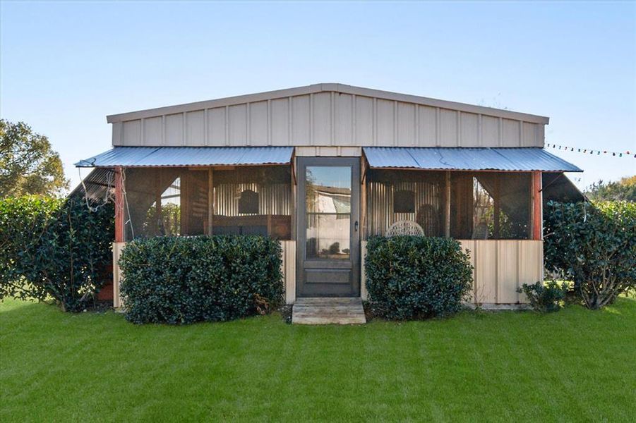 View of front of gameroom featuring a sunroom, a front lawn, a metal roof, and board and batten siding View of front of gameroom featuring a sunroom, a front lawn, a metal roof, and board and batten siding