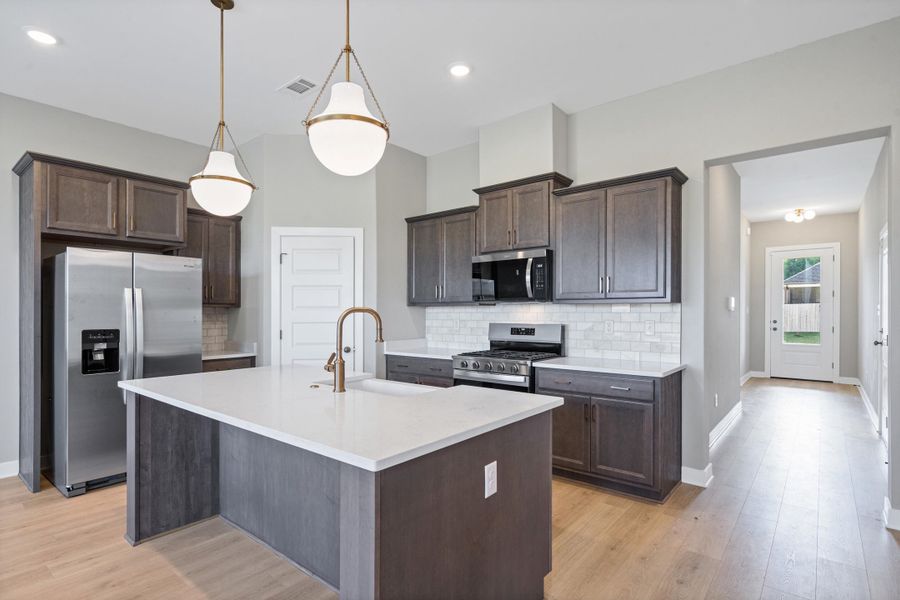 Kitchen featuring an island with white countertop, dark wood-finish cabinetry, stainless steel appliances, and a white subway tile backsplash