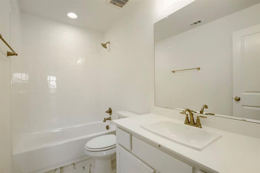 Bathroom featuring a white vanity with integrated sink, a large wall-mounted mirror, brushed bronze fixtures, and white subway tile surround in the tub and shower area