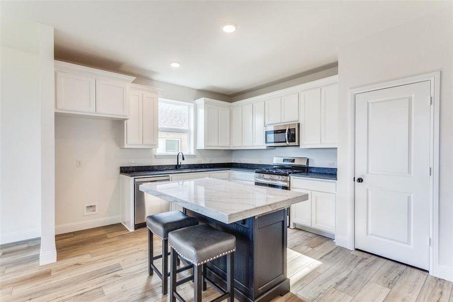 Kitchen with light wood-type flooring, white cabinets, a kitchen island, stainless steel appliances, and sink