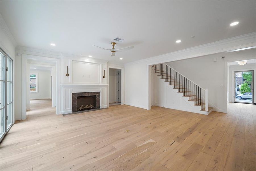 Spacious living area with a cozy fireplace, elegant wooden floors, and a modern stairway leading upstairs, viewed from the kitchen's perspective.