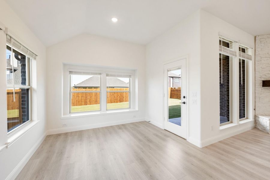 Empty living room with light wood floors, vaulted ceiling, large windows, and glass back door Empty living room with light wood floors, vaulted ceiling, large windows, and glass back door