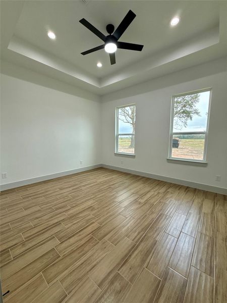 This room features light wood like tile flooring, a tray ceiling with recessed lighting, and a modern ceiling fan. It has large windows offering plenty of natural light and a view of the outdoors. This room features light wood like tile flooring, a tray ceiling with recessed lighting, and a modern ceiling fan. It has large windows offering plenty of natural light and a view of the outdoors.