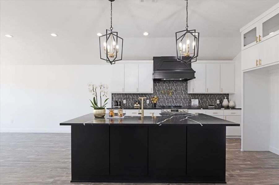 Kitchen featuring glass insert cabinets, a kitchen island with sink, white cabinets, and hanging light fixtures