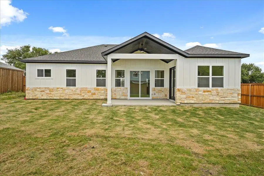 Rear exterior featuring a covered patio, board and batten siding, stone veneer accents, and a dark shingled roof