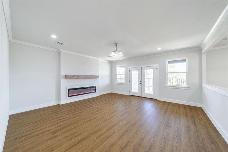 Unfurnished living room featuring ornamental molding, wood finished floors, a glass covered fireplace, french doors, and recessed lighting Unfurnished living room featuring ornamental molding, wood finished floors, a glass covered fireplace, french doors, and recessed lighting