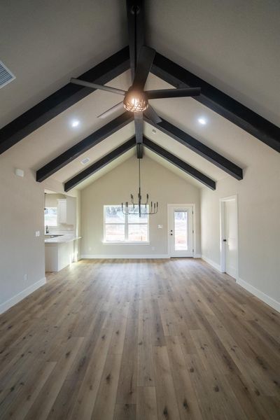 Unfurnished living room with wood finished floors, visible vents, baseboards, lofted ceiling with beams, and ceiling fan