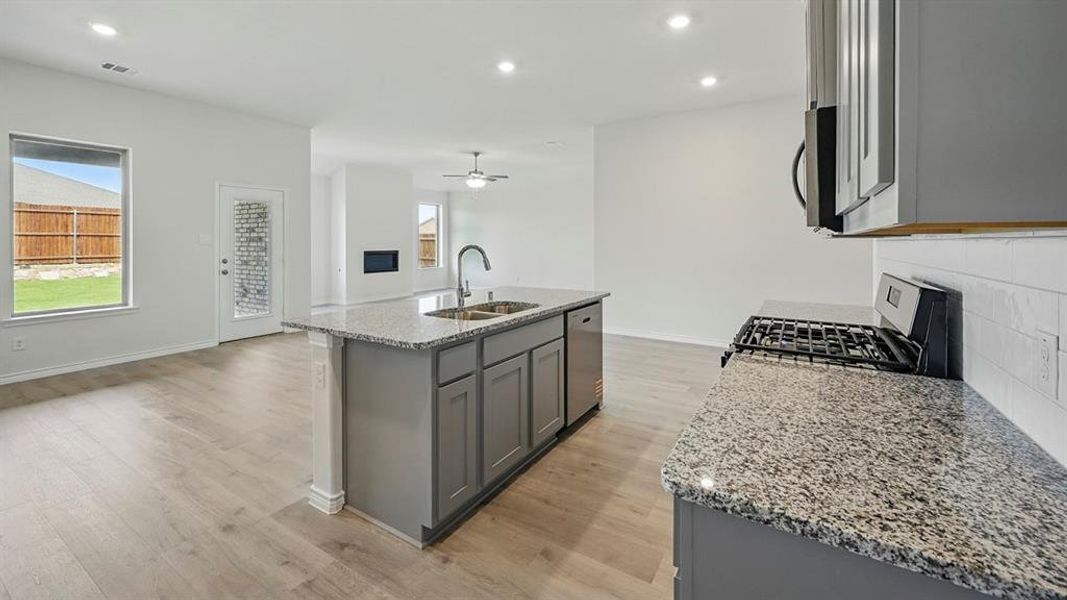 Kitchen with gray cabinetry, light stone countertops, appliances with stainless steel finishes, a kitchen island with sink, and recessed lighting