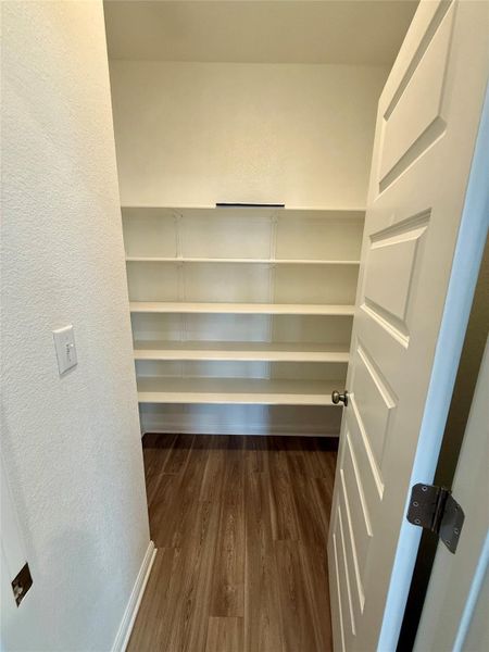 Spacious pantry with multiple white built-in shelving units, wood-finish flooring, and a white panel door with a dark bronze knob