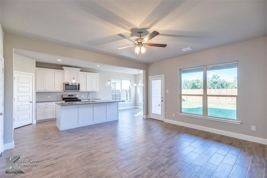 Kitchen featuring white cabinetry, wood finish floors, open floor plan, stainless steel appliances, and a center island with sink