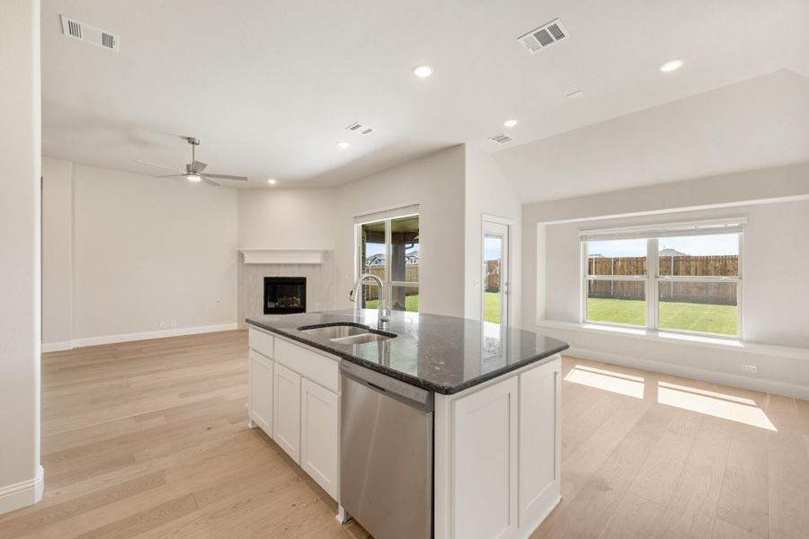 Kitchen island with dark granite countertop and sink, open to living area with fireplace and hardwood floors Kitchen island with dark granite countertop and sink, open to living area with fireplace and hardwood floors