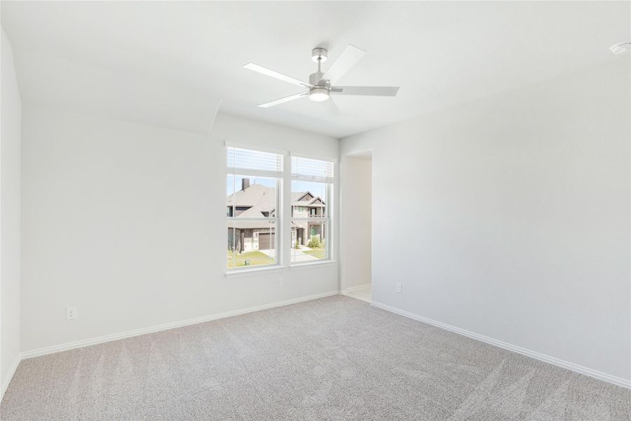 Empty bedroom with carpet flooring, ceiling fan, and double window overlooking neighborhood homes