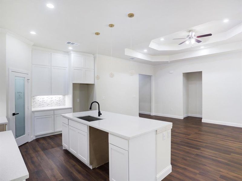 Kitchen with white cabinetry, a center island with sink, decorative light fixtures, dark wood finished floors, and ceiling fan Kitchen with white cabinetry, a center island with sink, decorative light fixtures, dark wood finished floors, and ceiling fan