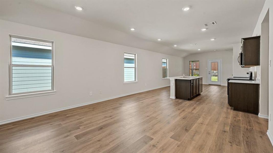Open-concept living space featuring wood-finish flooring, recessed lighting, and a kitchen island with integrated sink