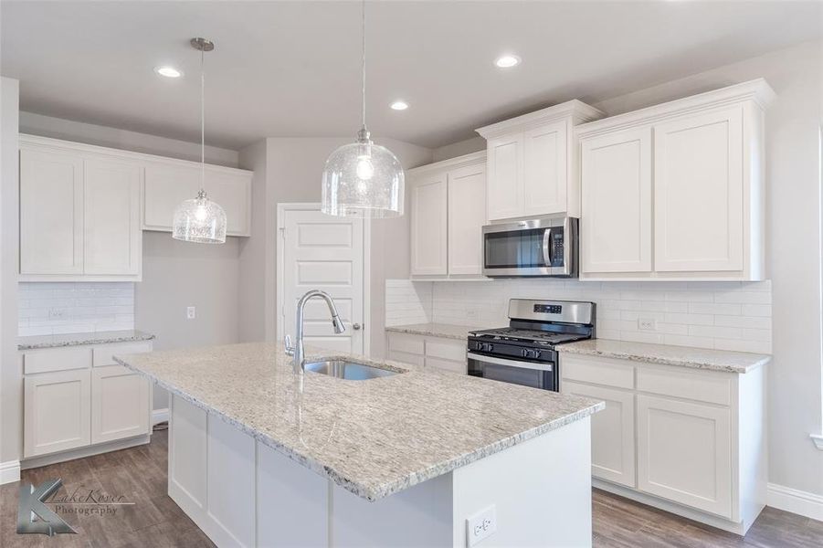 Kitchen with backsplash, stainless steel appliances, white cabinets, decorative light fixtures, and dark wood finish ceramic tile floors