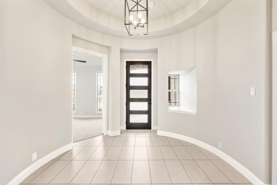 Rounded foyer with tray ceiling, pendant light, dark front door with glass panels, and tile floors Rounded foyer with tray ceiling, pendant light, dark front door with glass panels, and tile floors