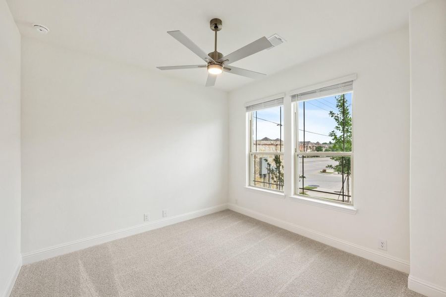 Empty bedroom with ceiling fan, carpet flooring, and two windows with neighborhood view