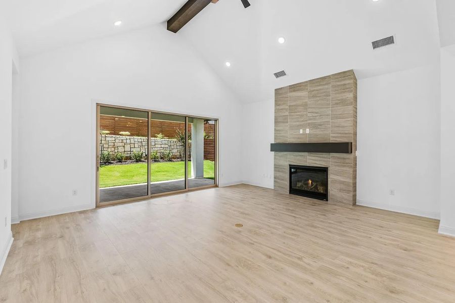 Unfurnished living room with beam ceiling, light wood-style floors, high vaulted ceiling, a tile fireplace, and recessed lighting
