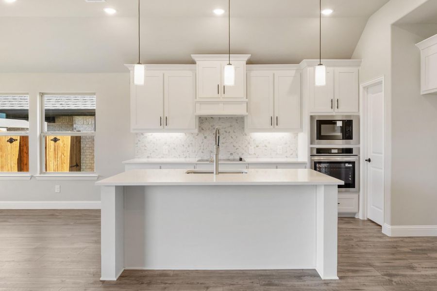 Kitchen with white cabinets, large island, pendant lights, tile backsplash, and stainless steel appliances on wood floors Kitchen with white cabinets, large island, pendant lights, tile backsplash, and stainless steel appliances on wood floors