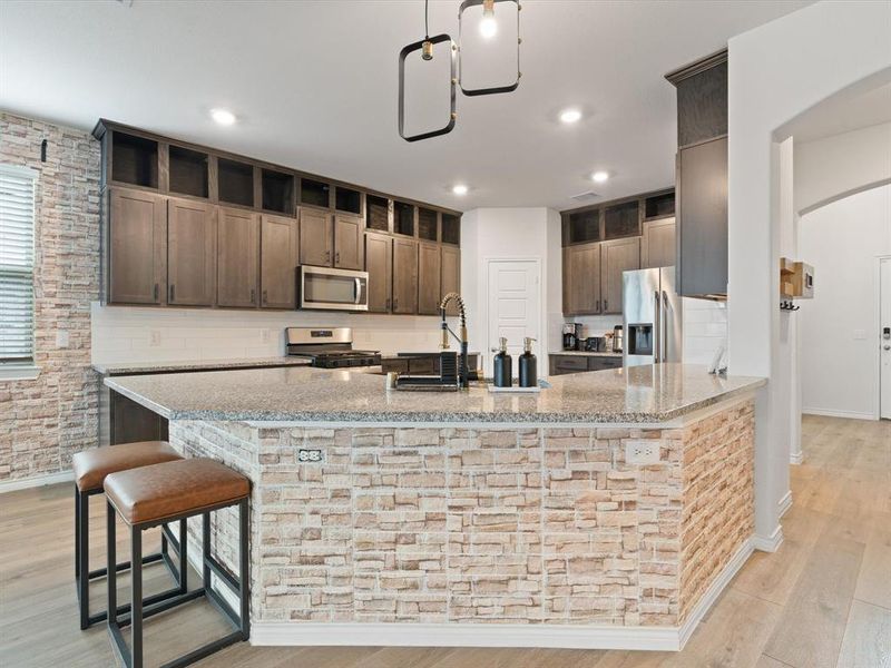 Kitchen with stainless steel appliances, light stone countertops, light wood-type flooring, and kitchen peninsula