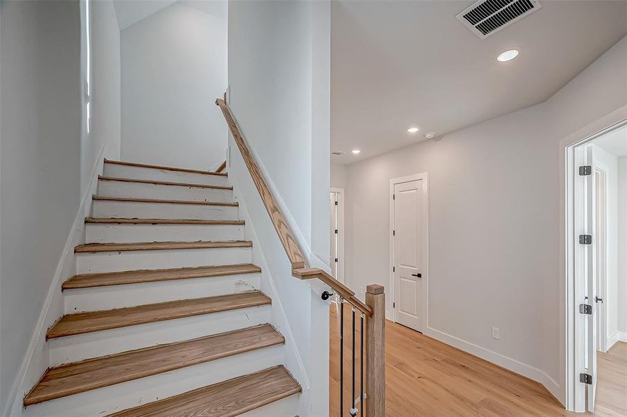 This photo shows a modern, well-lit interior hallway with light wood flooring and a staircase leading to the upper floor. The walls are painted in a neutral color, and recessed lighting is installed in the ceiling. Doors to adjacent rooms are visible, offering a spacious and inviting atmosphere.