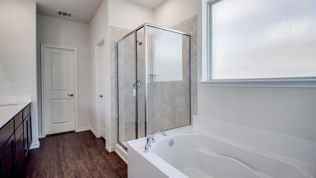 Full bath with dark wood-style flooring, vanity, a stall shower, and a garden tub Full bath with dark wood-style flooring, vanity, a stall shower, and a garden tub
