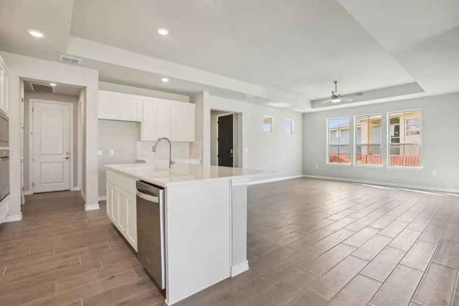 Kitchen with a raised ceiling, white cabinets, wood tiled floors, light stone countertops, and a center island with sink