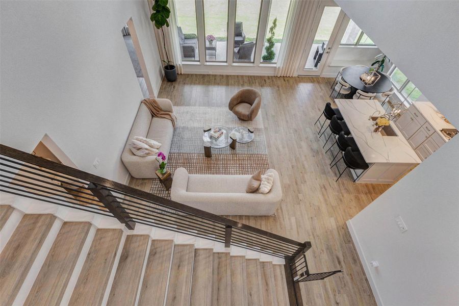 Modern, open-concept living area with hardwood looking floors, a cozy seating arrangement, and a stylish kitchen island with bar seating. Large windows offer plenty of natural light, enhancing the spacious feel. The view from the staircase highlights the inviting layout, ideal for entertaining and family gatherings. Modern, open-concept living area with hardwood looking floors, a cozy seating arrangement, and a stylish kitchen island with bar seating. Large windows offer plenty of natural light, enhancing the spacious feel. The view from the staircase highlights the inviting layout, ideal for entertaining and family gatherings.