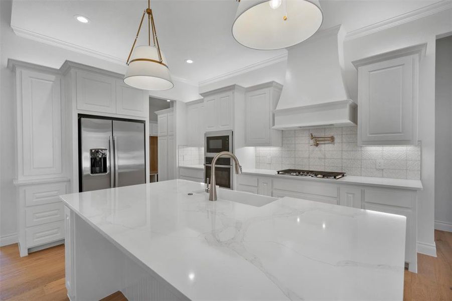 Kitchen featuring light stone countertops, stainless steel appliances, light hardwood / wood-style flooring, decorative light fixtures, and custom exhaust hood