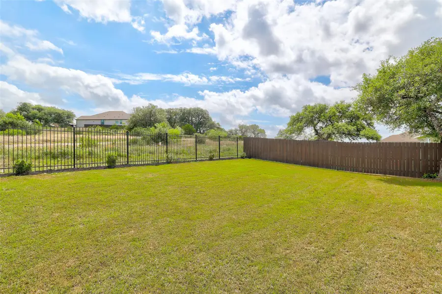 Expansive green lawn with a dark wood privacy fence and a black metal fence bordering natural landscaping