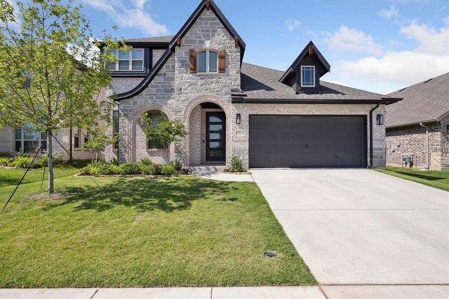 French provincial home with brick siding, an attached garage, a front yard, driveway, and stone siding