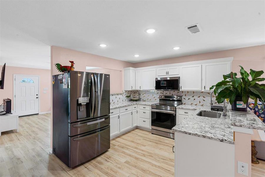 Kitchen with appliances with stainless steel finishes, white cabinetry, a peninsula, light stone counters, and recessed lighting Kitchen with appliances with stainless steel finishes, white cabinetry, a peninsula, light stone counters, and recessed lighting