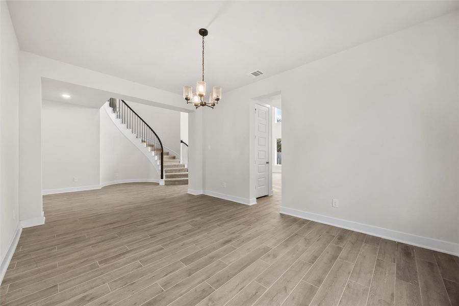 Bright, spacious room with wood-look porcelain tile flooring and modern chandelier. Features an elegant, curved staircase and a doorway leading to another well-lit area. Perfect for a welcoming entry or living space. Bright, spacious room with wood-look porcelain tile flooring and modern chandelier. Features an elegant, curved staircase and a doorway leading to another well-lit area. Perfect for a welcoming entry or living space.